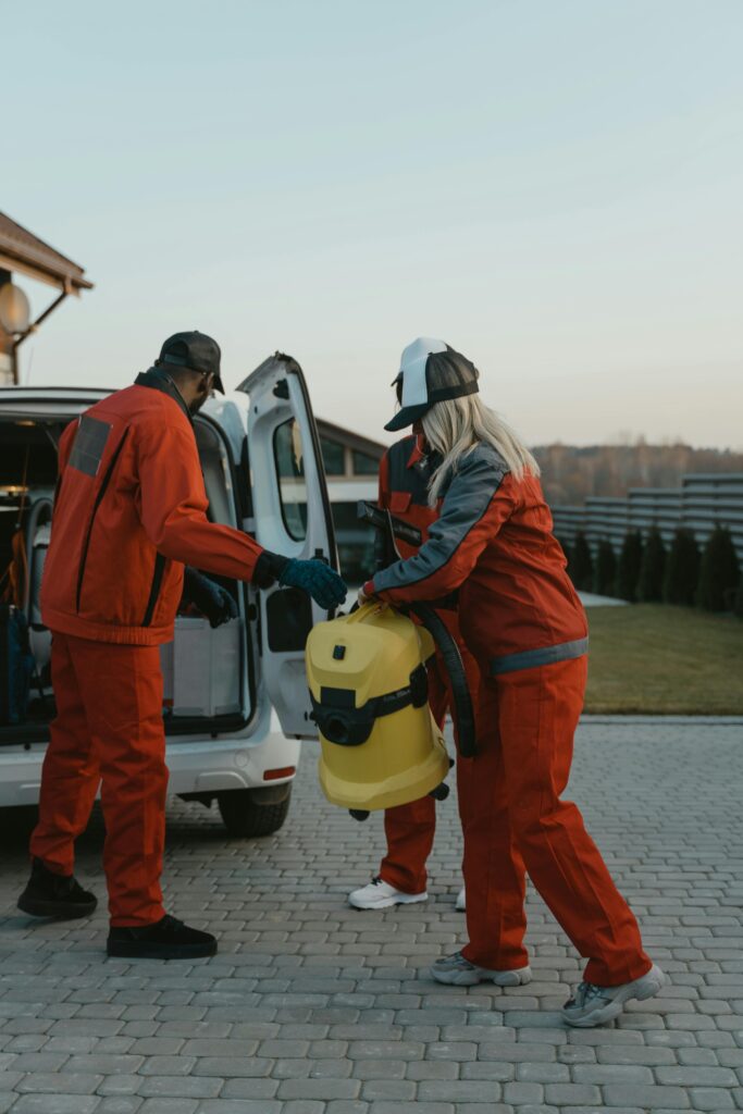 Workers in uniforms load outdoor equipment into a van on a sunny day.