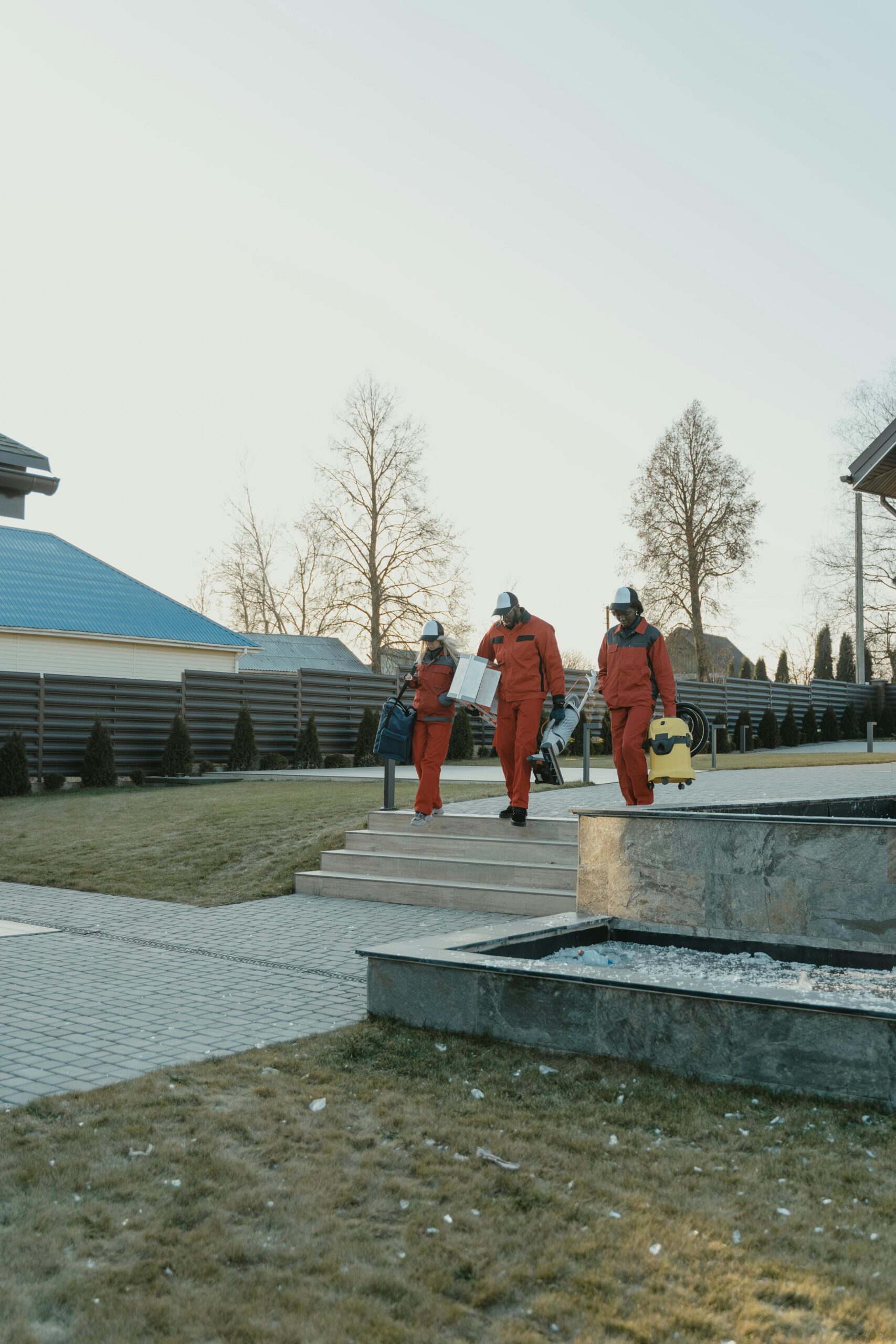 Workers in protective suits and helmets perform outdoor sanitation tasks in a residential area.